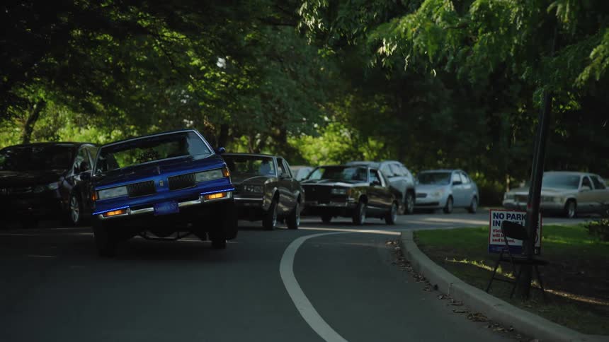 Blue car lifting its front end while driving down a treelined street