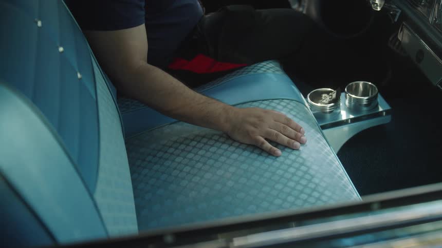 Arm in dark shirt rests on blue vintage car seat with metallic center console