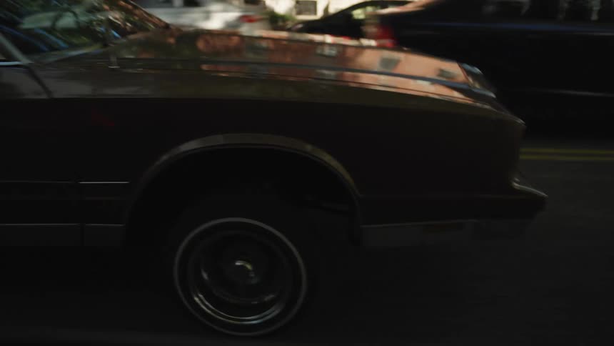 Brown car with raised suspension driving down an urban street during the day