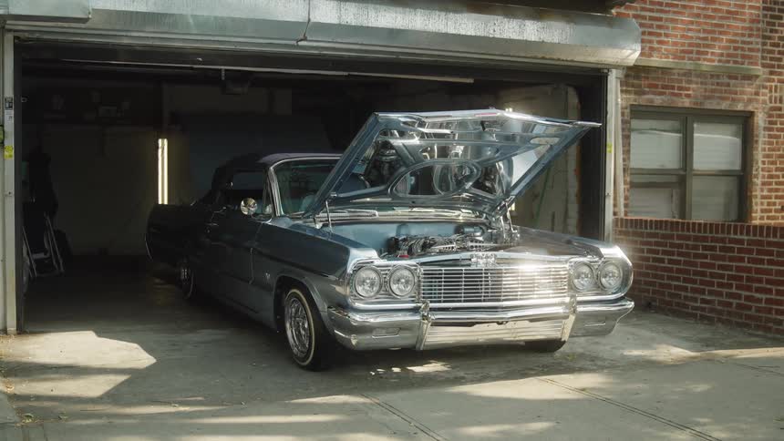 Silver classic car with the hood open parked in a residential garage