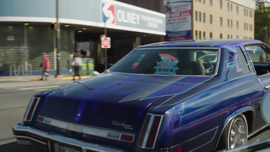 Customized classic car in blue and purple drives with raised rear near olney terminal
