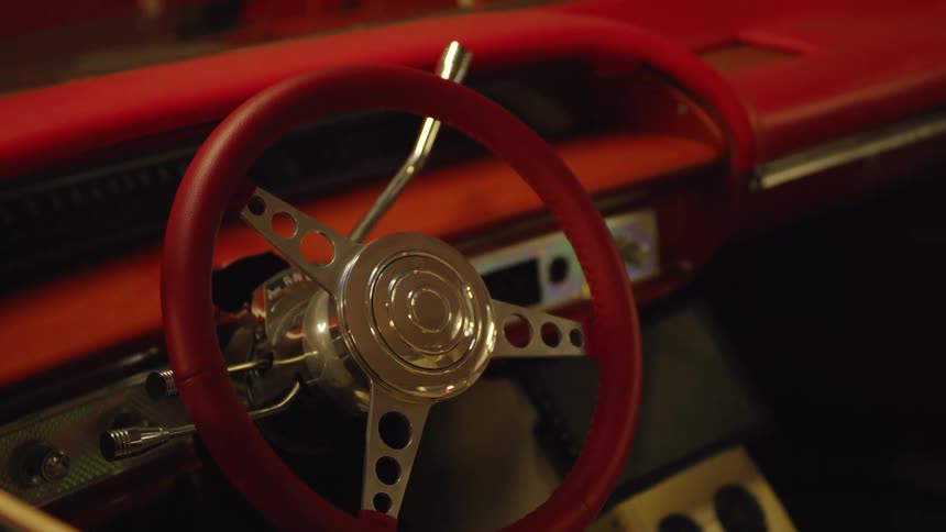 A car with a red interior features a steering wheel accented in red and gold at midday