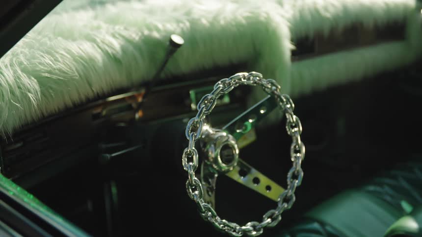 The video is an extreme closeup of a cars interior featuring an unusual chrome steering wheel made of chain links the dashboard and seating area are covered in fuzzy light green or mintcolored shag material