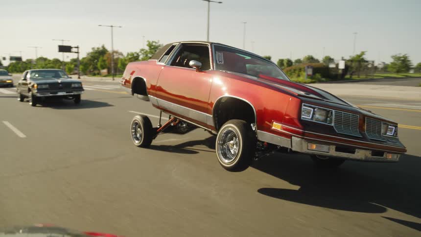 Red car with front hydraulic suspension lifted on a treelined street