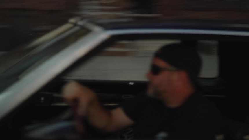 Classic car with raised suspension driving through urban street lined with brick buildings