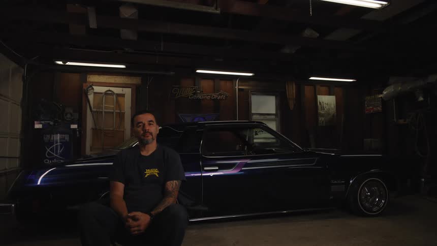 Man sitting in a garage beside a classic black car