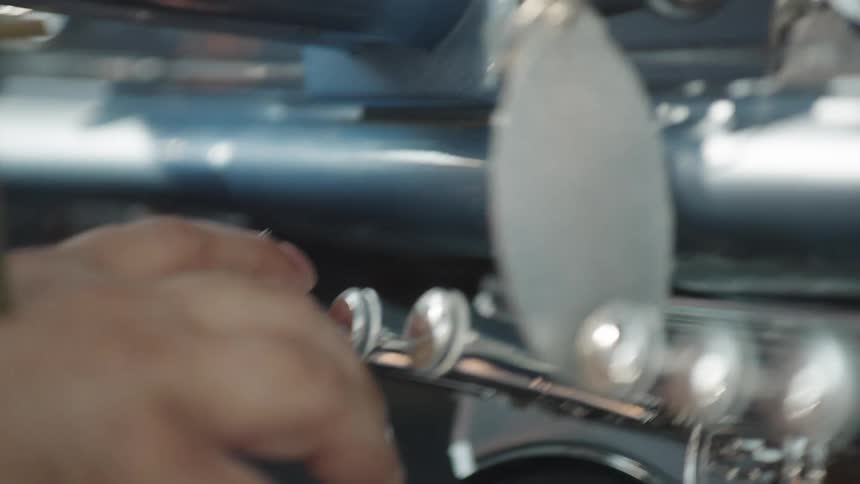 Fingers pressing the valves of a silver trumpet under natural light