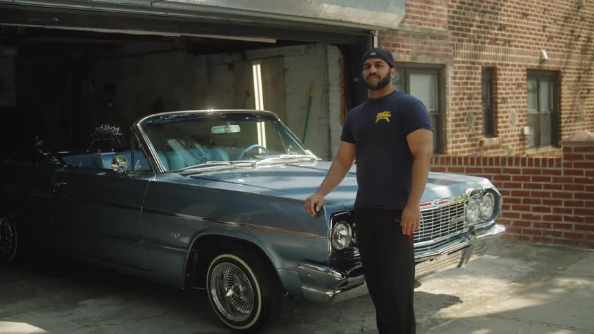 Man stands beside a classic blue lowrider partially parked in a garage