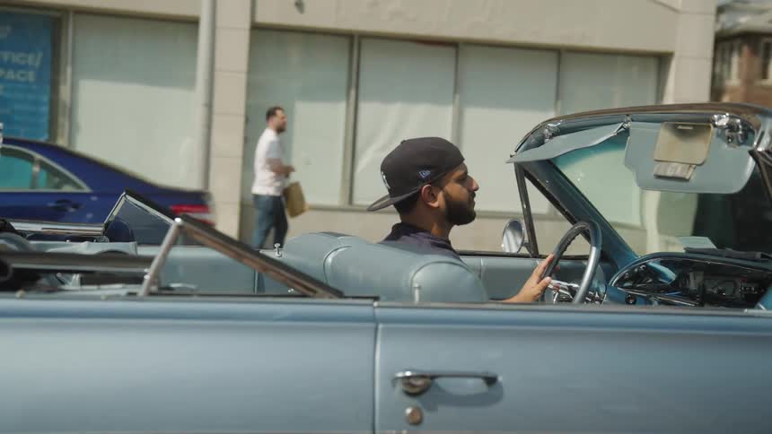 Man drives a blue convertible car through the city
