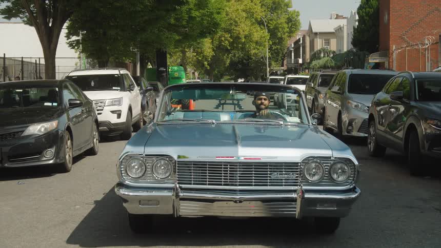 A young man driving a vintage car on a street in a suburban city during daytime