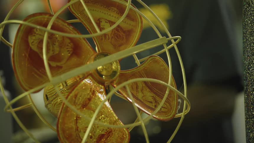A closeup of a vintage metal desk fan with ambertinted blades behind a gold wire cage