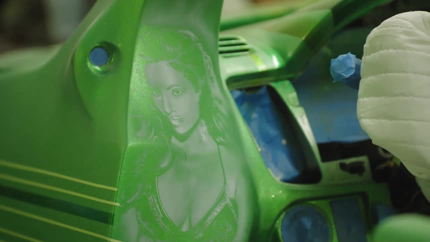 The video is an extreme closeup shot of a classic cars bright green hood or side panel a detailed airbrushed image of a womans face and dcolletage is visible on the panelthe video is an extreme closeup shot of a classic cars bright green