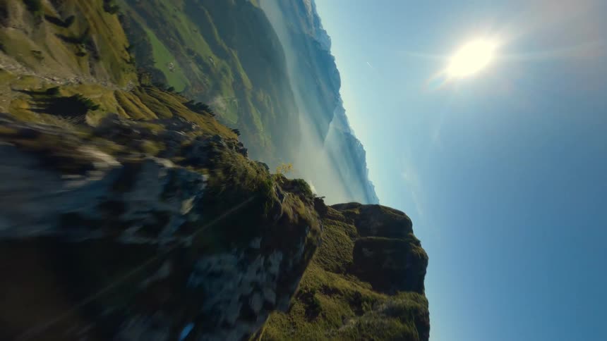 A grassy mountain ridge rises under a bright blue sky with distant haze