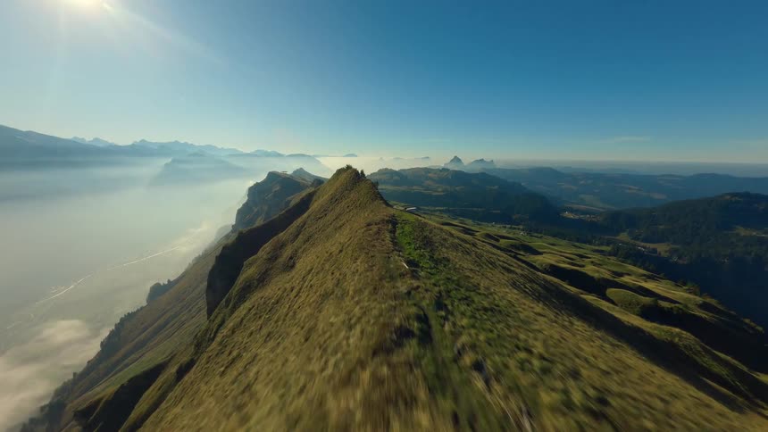 Trail along grassy mountain ridge under clear sky with mountain ranges in the distance