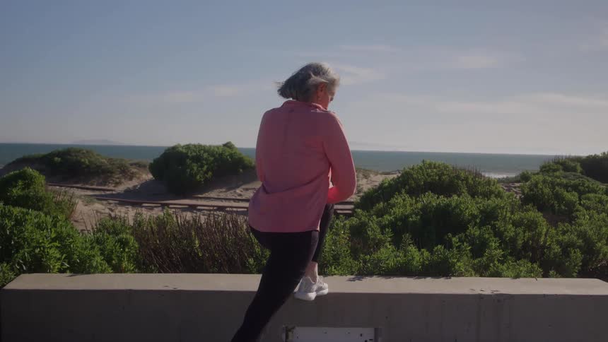 Person in athletic clothing looks at the sea beside a low wall during daytime