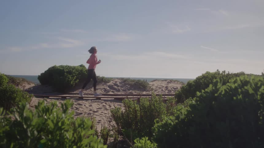 Woman running on a sandy trail surrounded by coastal vegetation