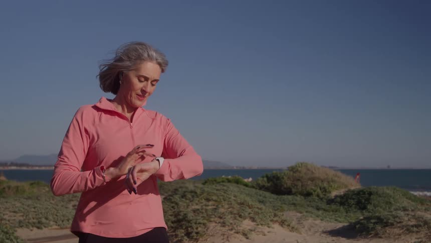 Woman adjusting earphones and watch and starting to run in coastal environment