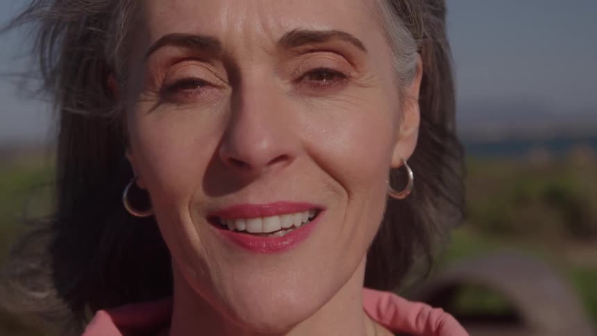 Grayhaired woman smiling under natural light in an outdoor setting