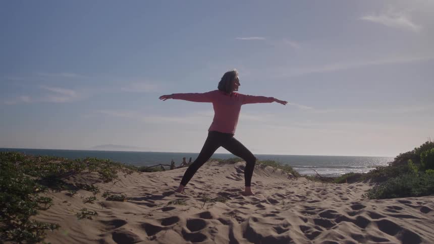 A young woman stretches barefoot on the beach under the bright sun