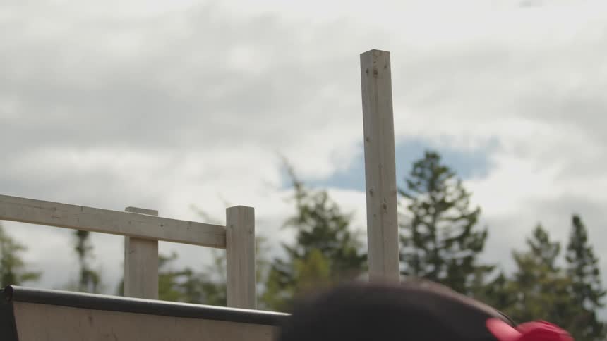 The video is a lowangle shot of a wooden skate or bike ramp structure against a bright overcast sky a person on a skateboard or bmx bike briefly comes into view from the bottom right as they fly off the ramp