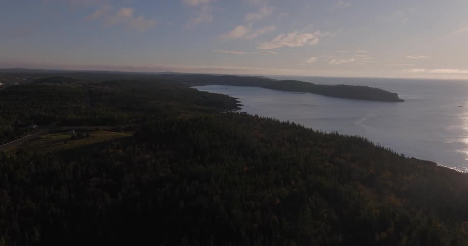 Dense forest borders the curved coastline under a partly cloudy sky at sunset