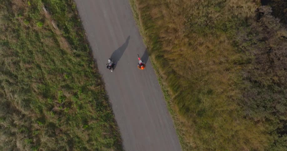 Two people ride their dirt bikes down the path on the field