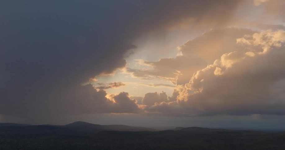 Golden light shines through storm clouds above a shadowed mountain range