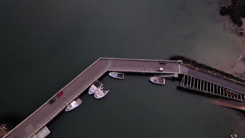 A bridge spans across a lake with boats docked nearby and cars parked along the roadside
