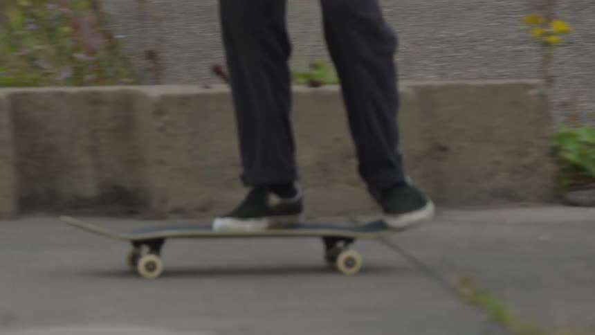 A skateboarder drops their board onto the pavement jumps on performs a kickflip and continues riding away in an urban industrial setting