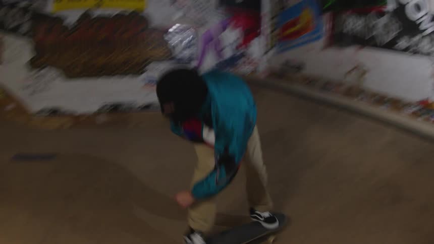 A masked man rides a skateboard on an indoor ramp at a skate park