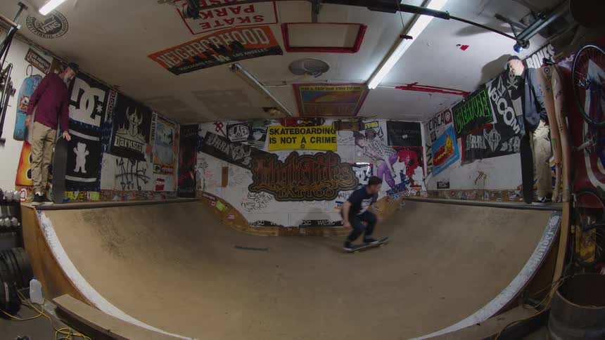 A man skateboarding on a ramp with two other men holding skateboards and watching