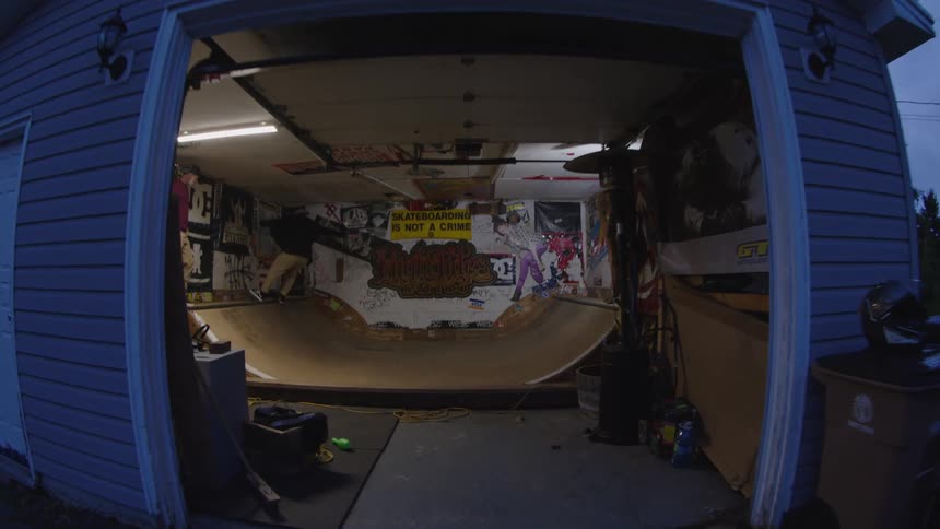 Wooden mini ramp fills indoor space decorated with posters and graffiti as person prepares for a trick
