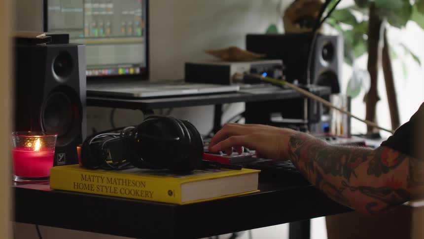 A person works on music equipment at a desk in a studio