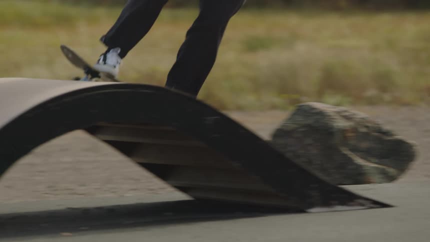 Skateboarder performs trick on waveshaped ramp in paved area with grass in the background