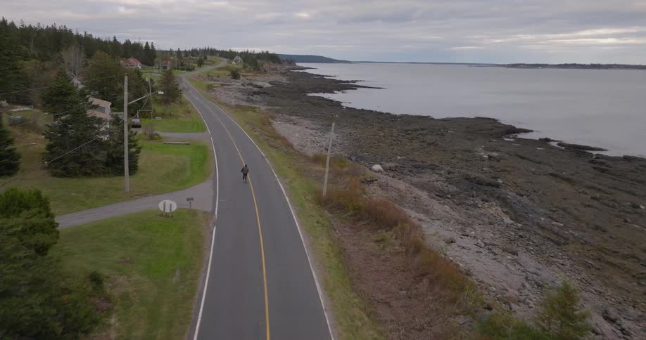 A man rides a skateboard along the middle of a suburban road at midday