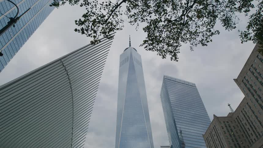 A tall modern skyscraper rises against a gray cloudy sky