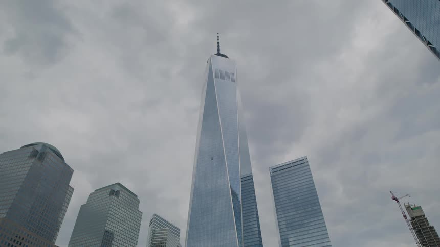The video features an upwardpanning shot of the one world trade center skyscraper towering over surrounding buildings in a city landscape likely new york city the sky is overcast and grey giving the scene a cool subdued lighting