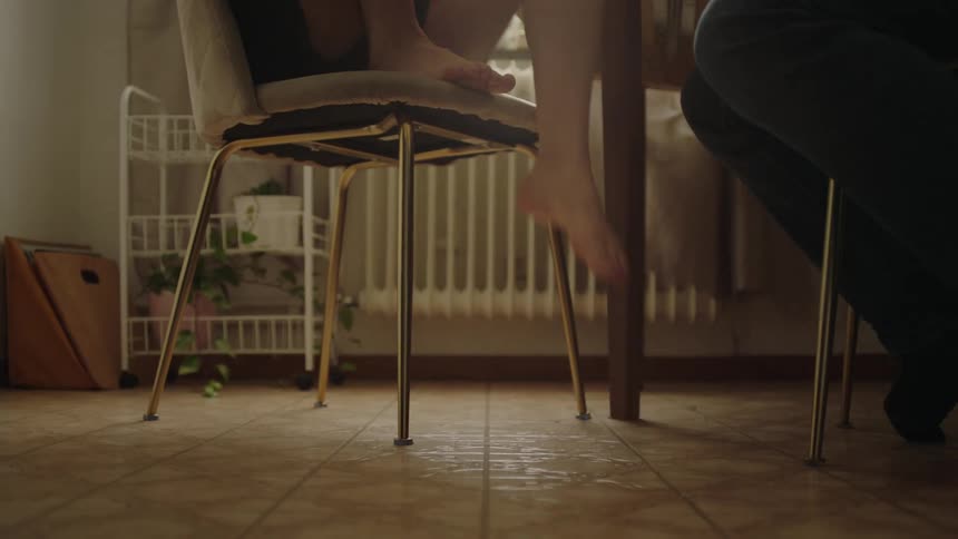 A low angle view of a dining area shows the legs of a child walking and sitting at a table with bare feet near the gold legs of a modern velvet chair on a tiled floor
