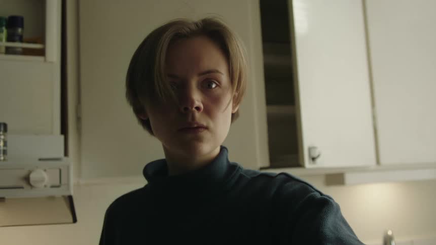 A young woman with short hair in a kitchen holding a knife and pointing it forward