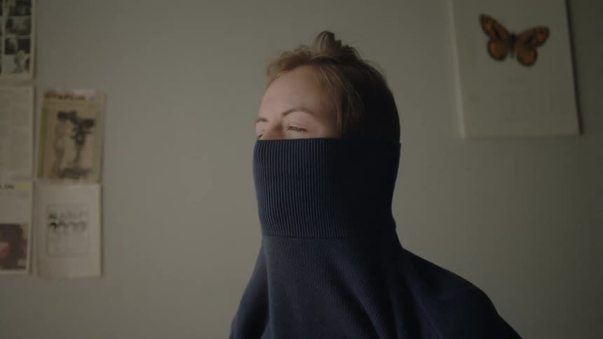 Person putting on a dark sweater in a softly lit room