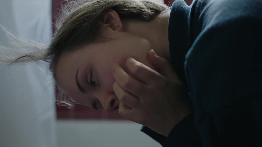 A young woman sits on a toilet seat appearing sad and disappointed