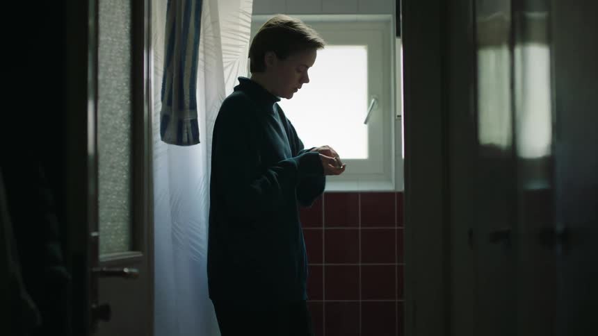 A young woman in pajamas walks into her bathroom at midday takes medicine from the counter swallows it and then walks out