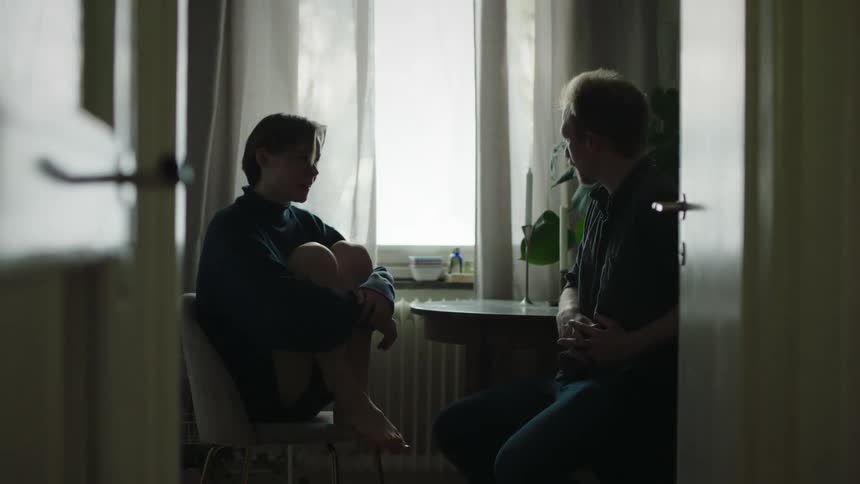Two people sitting in a room lit by natural light talking in front of a window