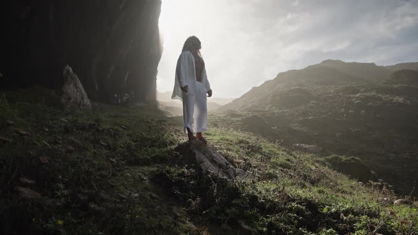 Person in a white robe standing on a rock in a sunlit valley