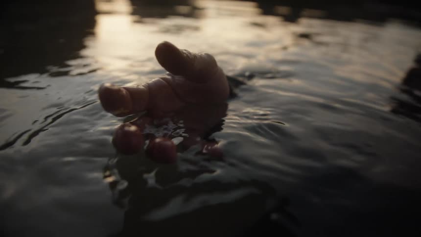 A hand rises dramatically from the dark rippling water toward the surface before submerging again