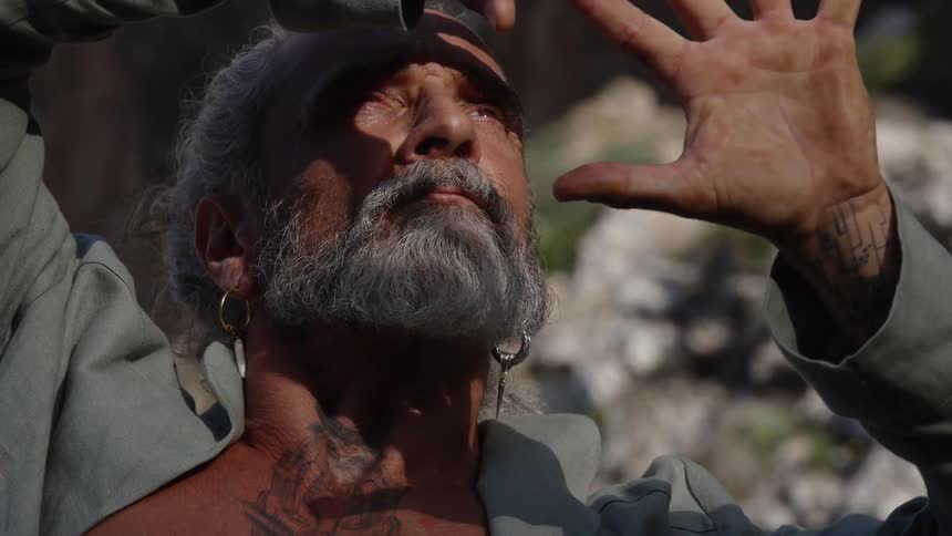 Man with a gray beard and neck tattoo looking upward under sunlight