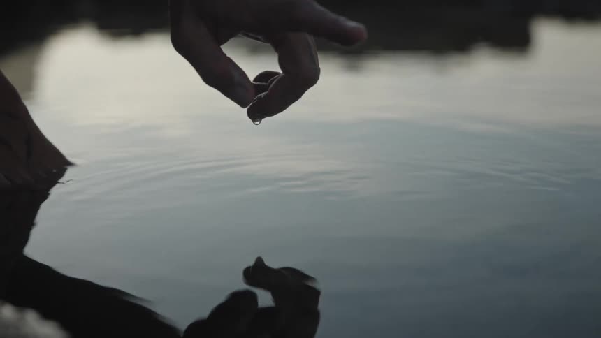 A persons finger gently touches the surface of an outdoor pool of water at sunset