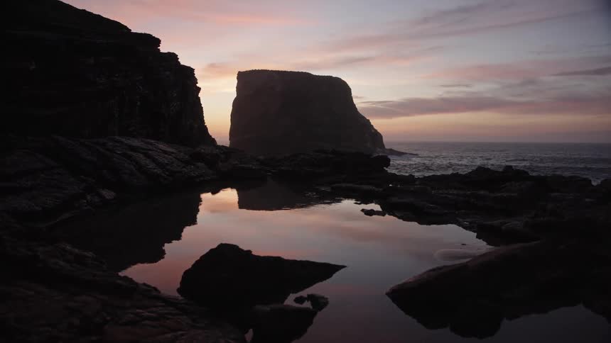 Heavy waves crash against a rocky shoreline at sunset