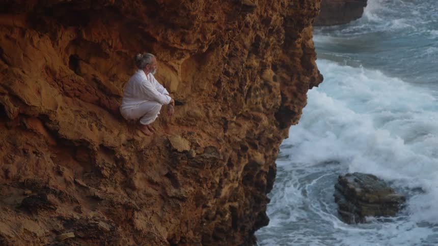 Person sitting on rocky cliff overlooking rough sea waves