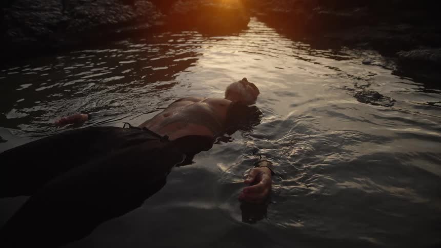An older man without a shirt wearing only pants floating in the water under the sunlight
